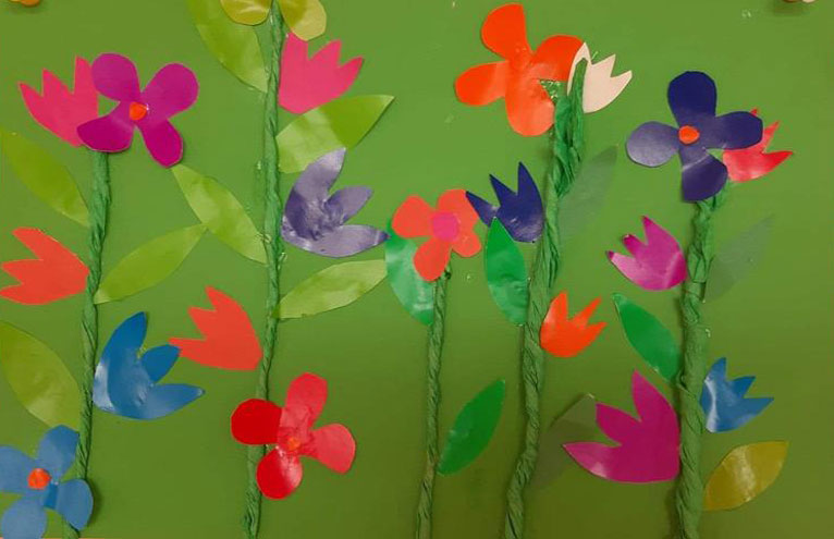 Zielone tło, róznokolorowe kwiaty z papieru wykonane przez świetliczaków.