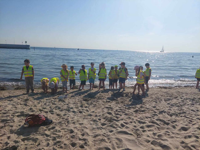 Plaża - grupa dzieci w kamizelkach odblaskowych.