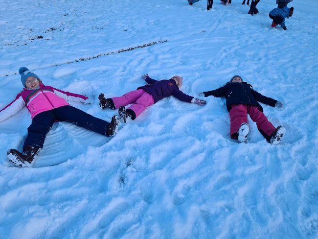 Trzy dziewczynki leżące na śniegu.