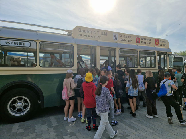 Grupa dzieci wsiadająca do zabytkowego trolejbusu.