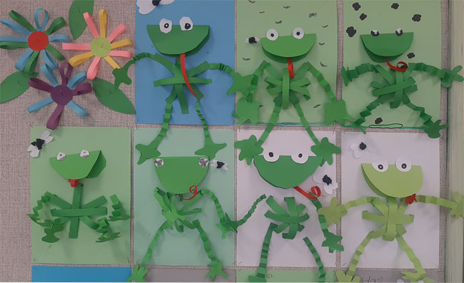 Prace dzieci - zielone papierowe żabki, kwiaty z pasków papieru.