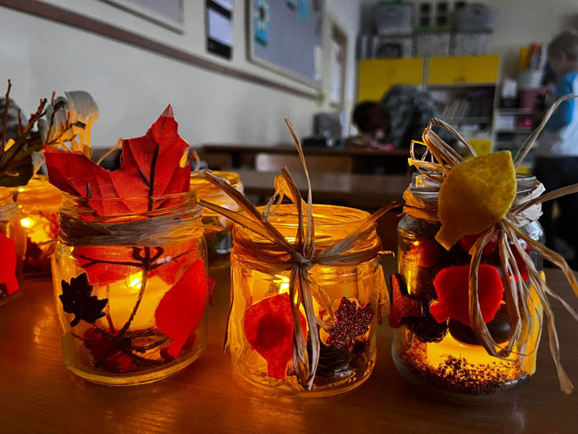 Świeczniki - szklane słoiki, palące się świeczki, kolorowe liście, brązowe wstążeczki.