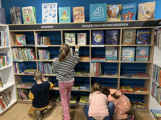 Biblioteka - dzieci przy regałach z książkami.