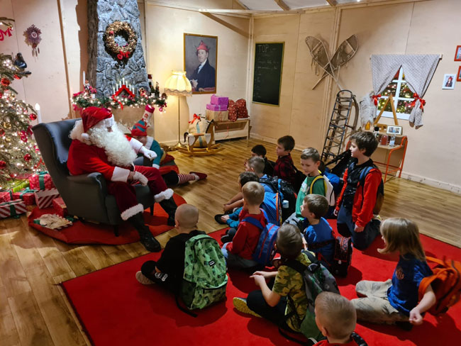 Mężczyzna w stroju Mikołaja, dzieci siedzące na dywanie.