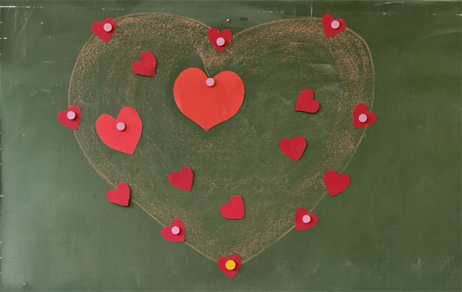 Zielona tablica - narysowane kredą żółte serce ozdobione czerwonymi serduszkami.